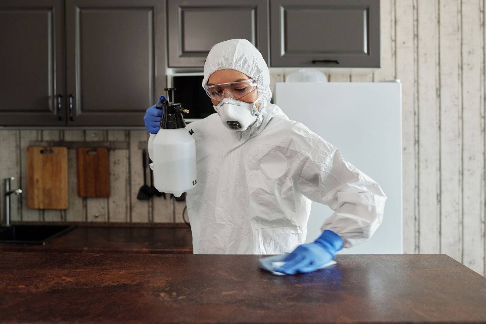 Technician in protective gear disinfecting a countertop with a pressure sprayer