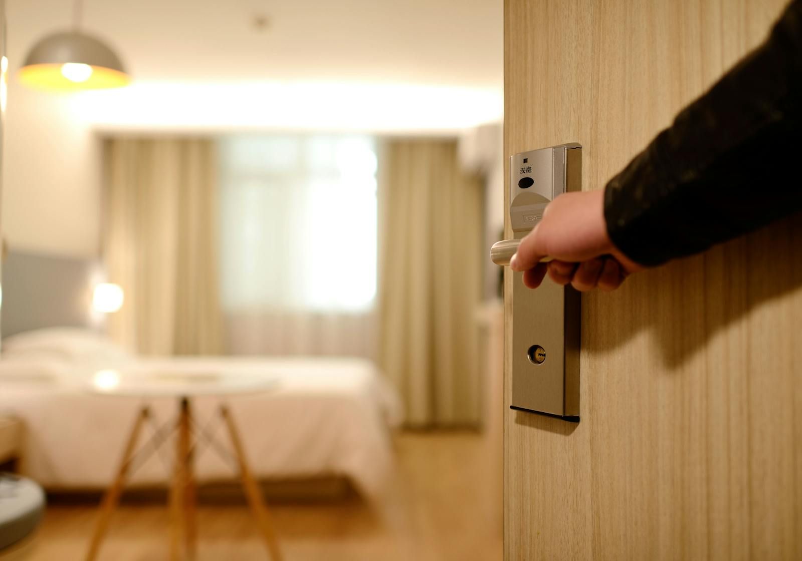 Hotel room door opening onto a freshly made bed